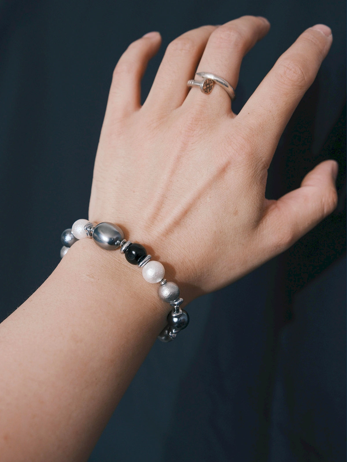 Quiet Rebel bracelet worn on the wrist against a dark background, with round beads and a reflective oval bead visible.