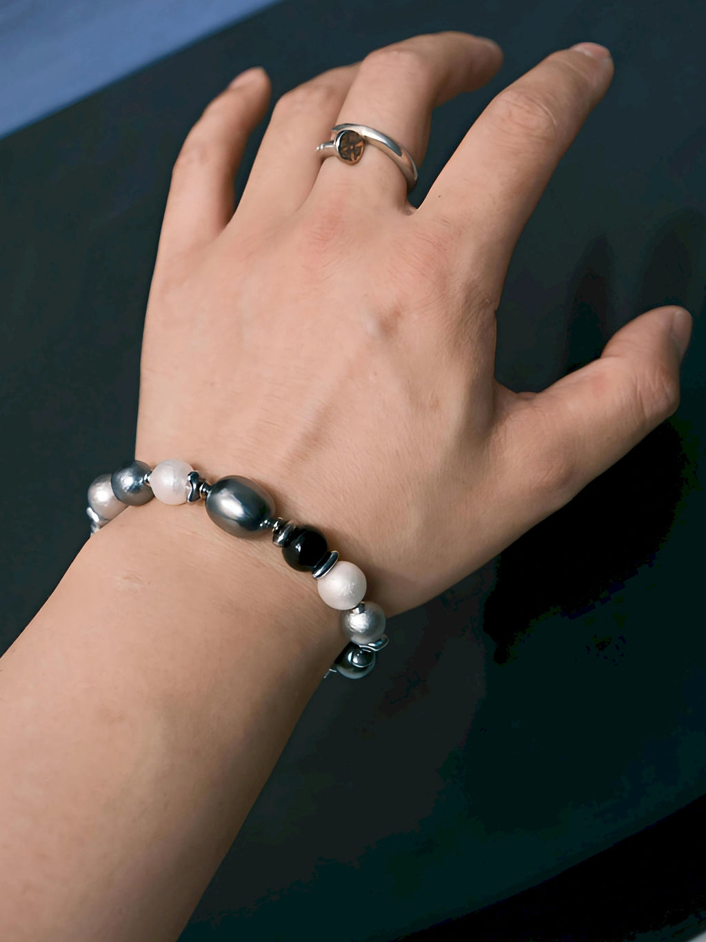 Angled on-wrist view of the Quiet Rebel bracelet, with white, dark and silver-tone beads beside a ring.