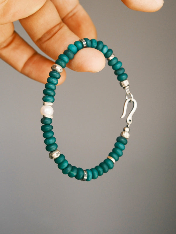 Forest Keeper green agate bracelet held between fingers, showing one white pearl, silver spacers and the open fishhook clasp.