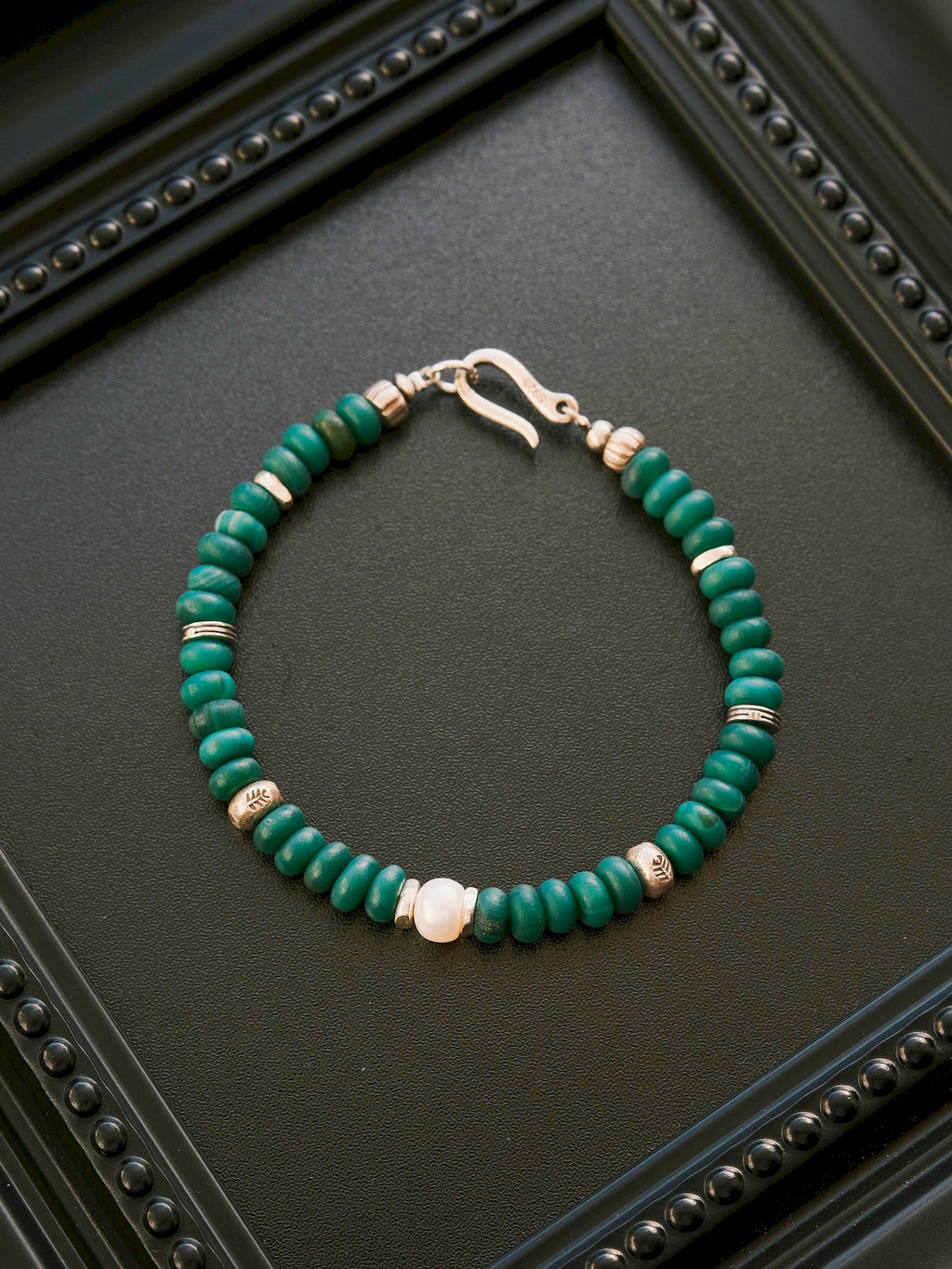 Forest Keeper green agate and pearl bracelet laid on a black framed display, with silver accents and a fishhook clasp.