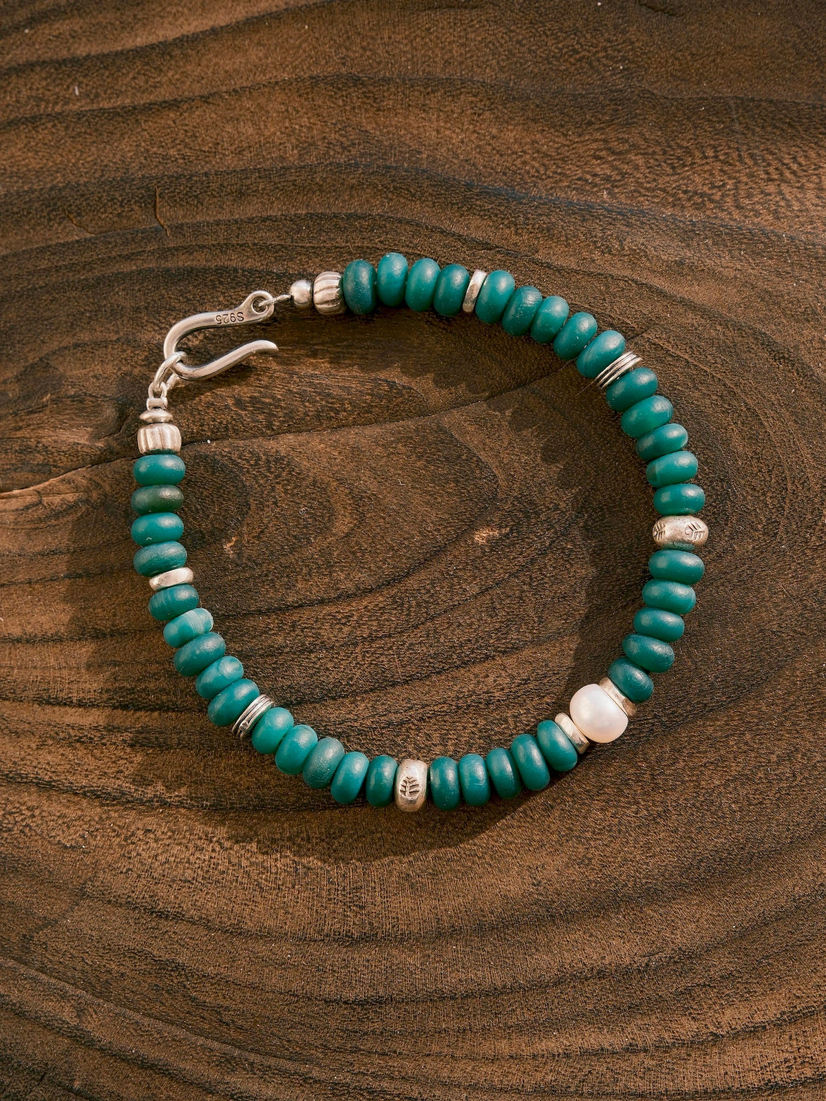 Forest Keeper bracelet on a wood-grain surface, showing green agate beads, one white pearl and silver spacer details.