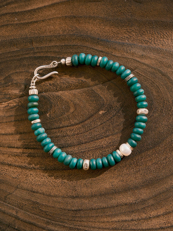 Forest Keeper bracelet on a wood-grain surface, showing green agate beads, one white pearl and silver spacer details.