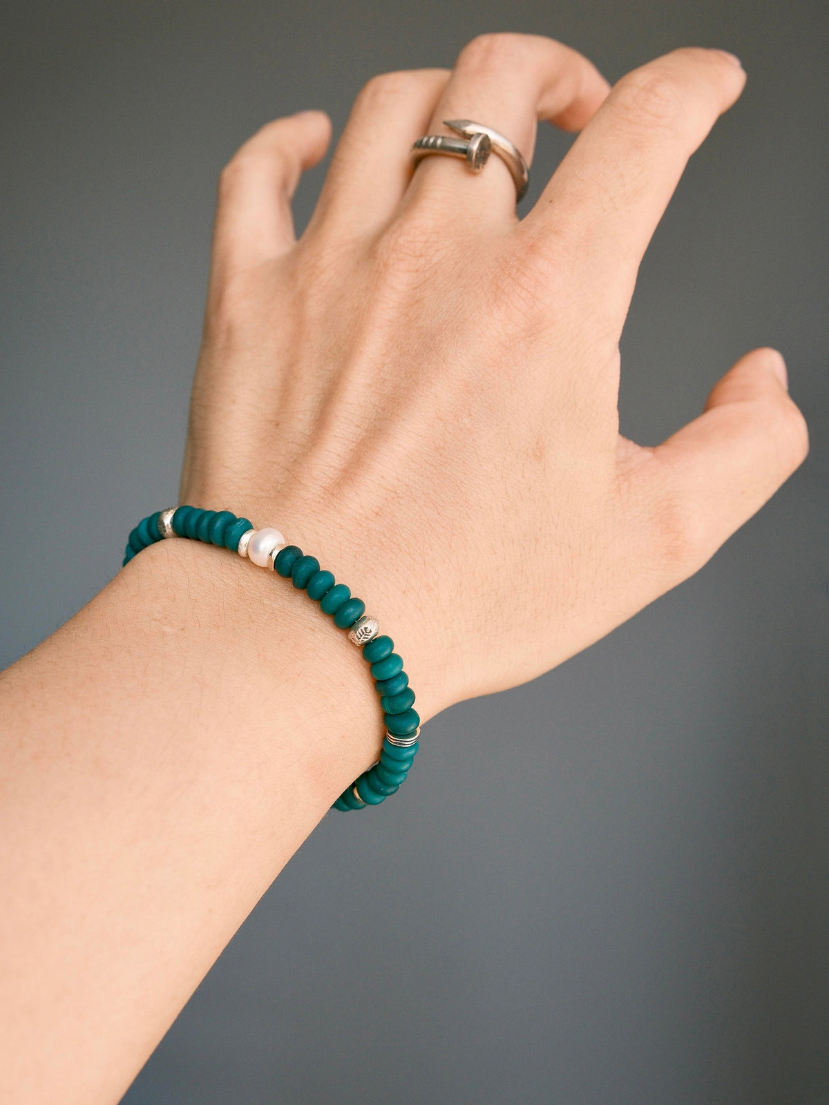 Forest Keeper green agate bracelet worn alone on the wrist, with one white pearl between silver spacers against a gray background.