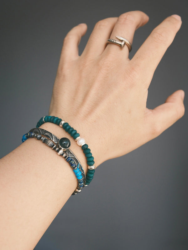 Forest Keeper green agate and pearl bracelet worn beside a silver-tone cuff and a blue beaded bracelet.