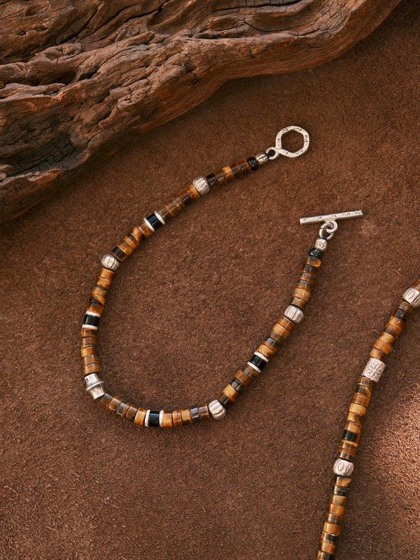 Open Umber Regent bracelet on a brown surface, with a toggle ring and bar and part of another bracelet at the right edge.