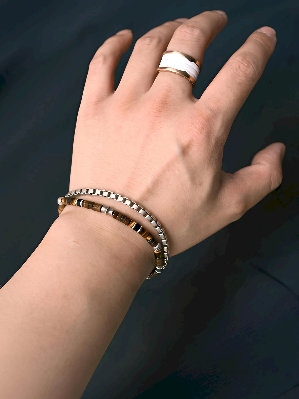 Angled wrist view of Umber Regent stacked with a separate silver-tone chain bracelet against a dark background.