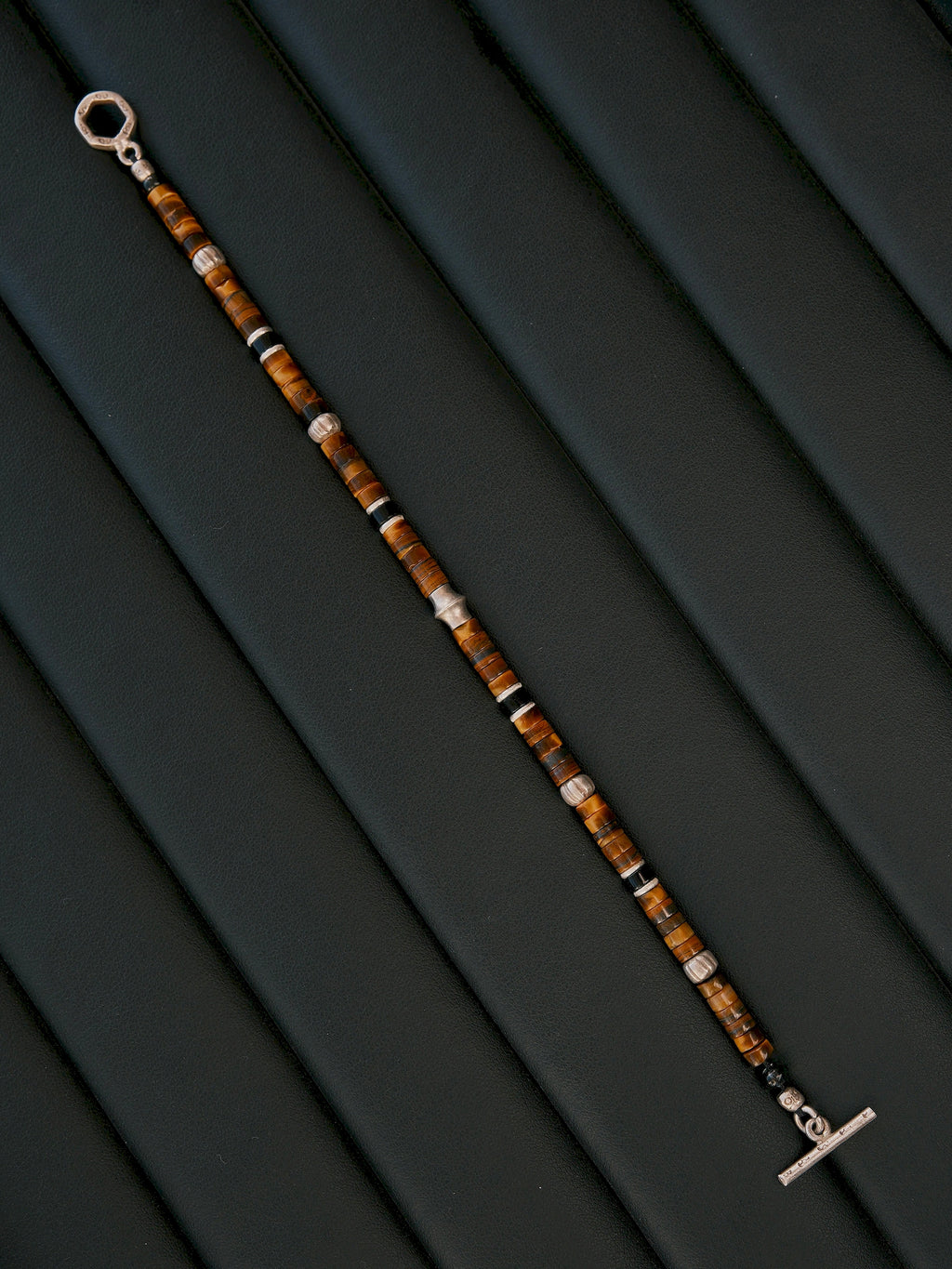 Umber Regent bracelet laid diagonally on dark upholstery, fully extended with the toggle ring and bar at opposite ends.