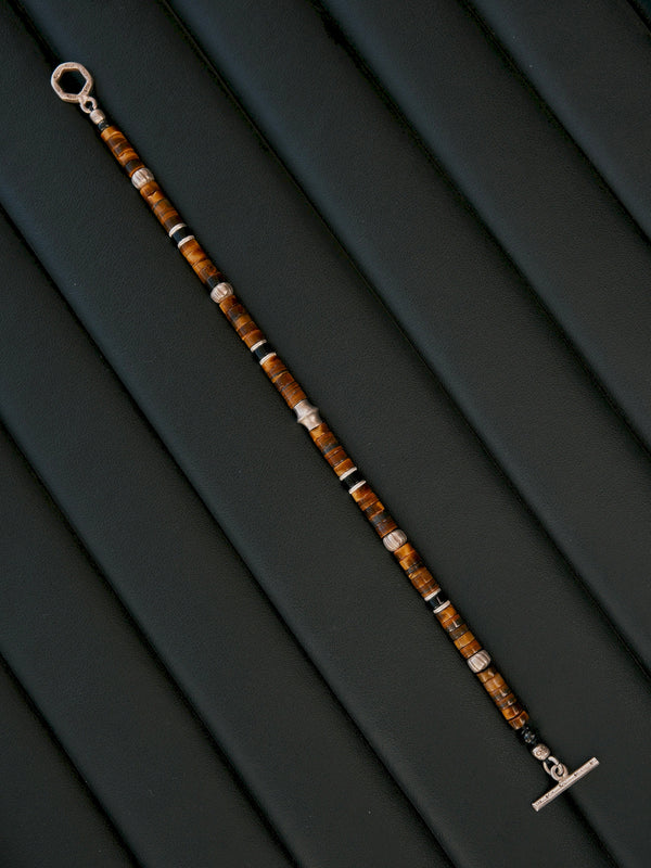 Umber Regent bracelet laid diagonally on dark upholstery, fully extended with the toggle ring and bar at opposite ends.
