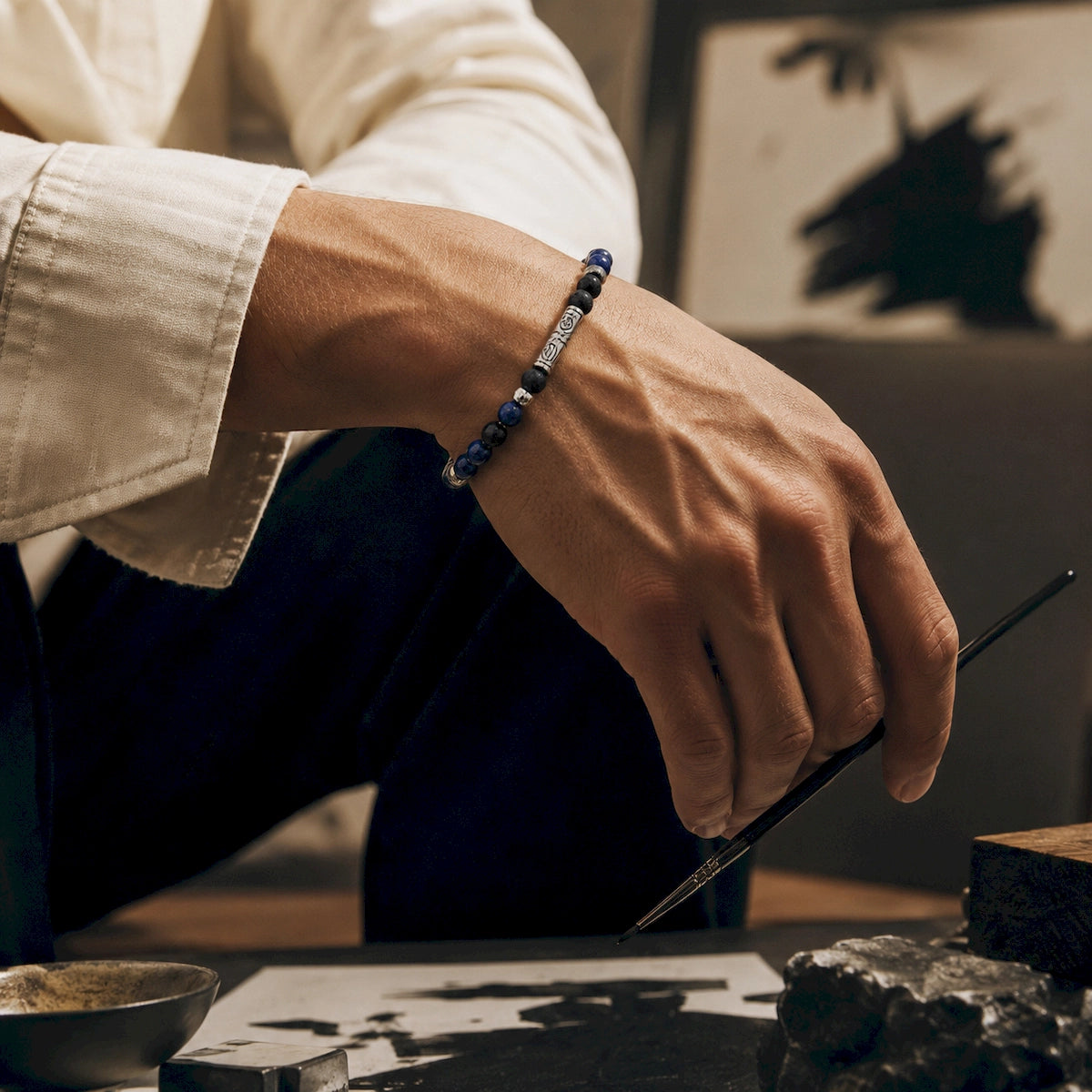 Creative man wearing a blue and black beaded bracelet while painting with an ink brush