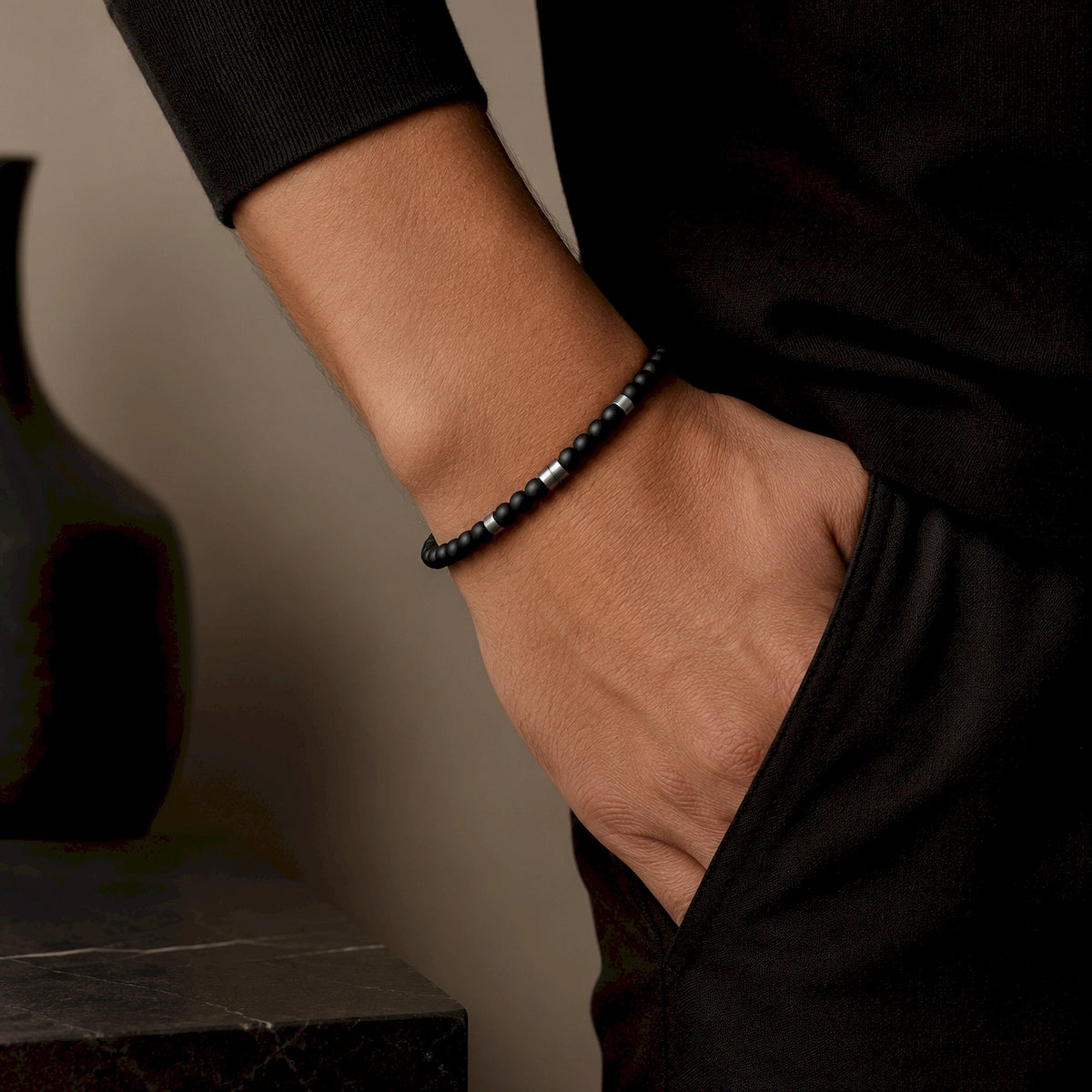 Minimalist black beaded bracelet with silver-tone spacers worn by a man dressed in black