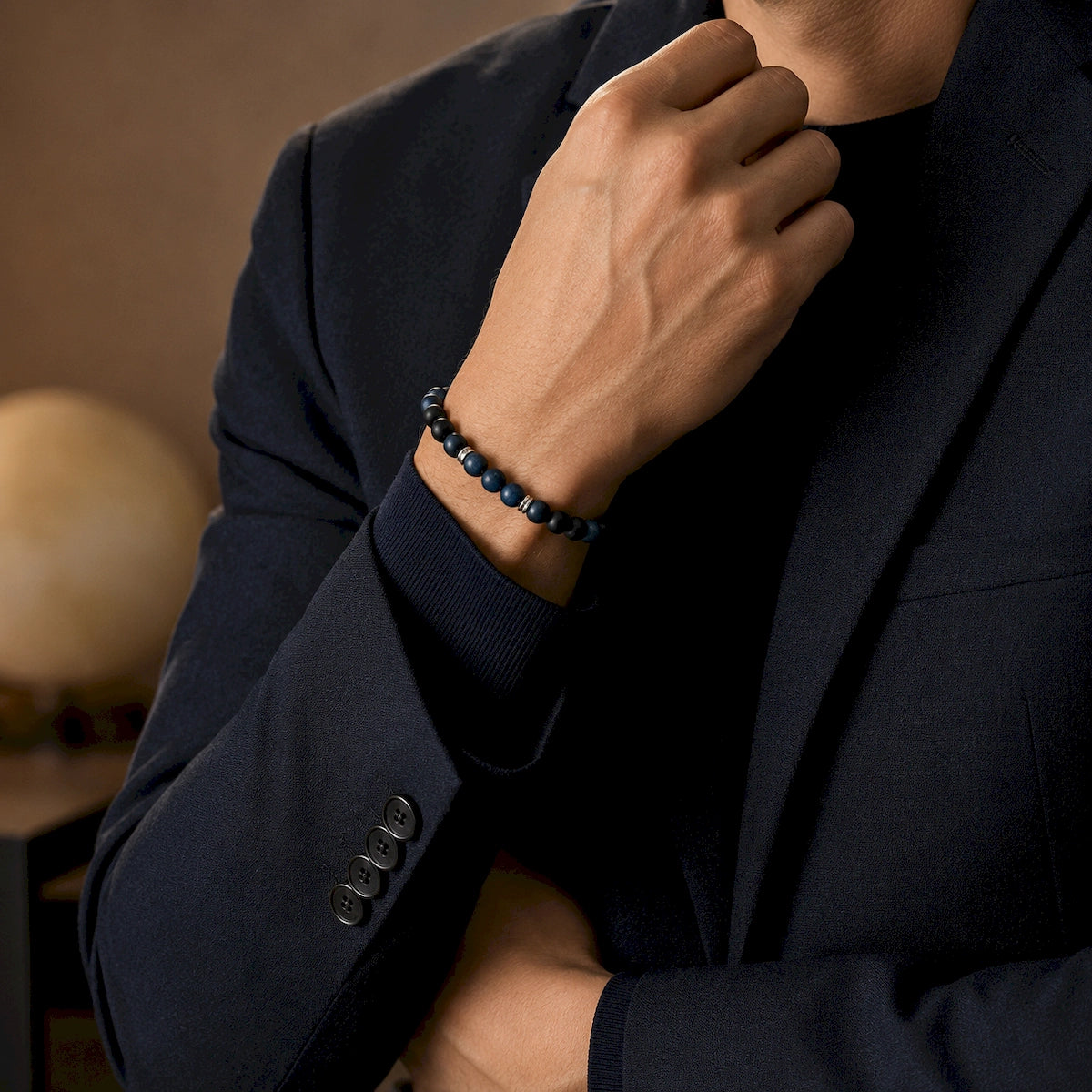 Man in a navy suit wearing a restrained blue and black beaded bracelet with silver-tone accents