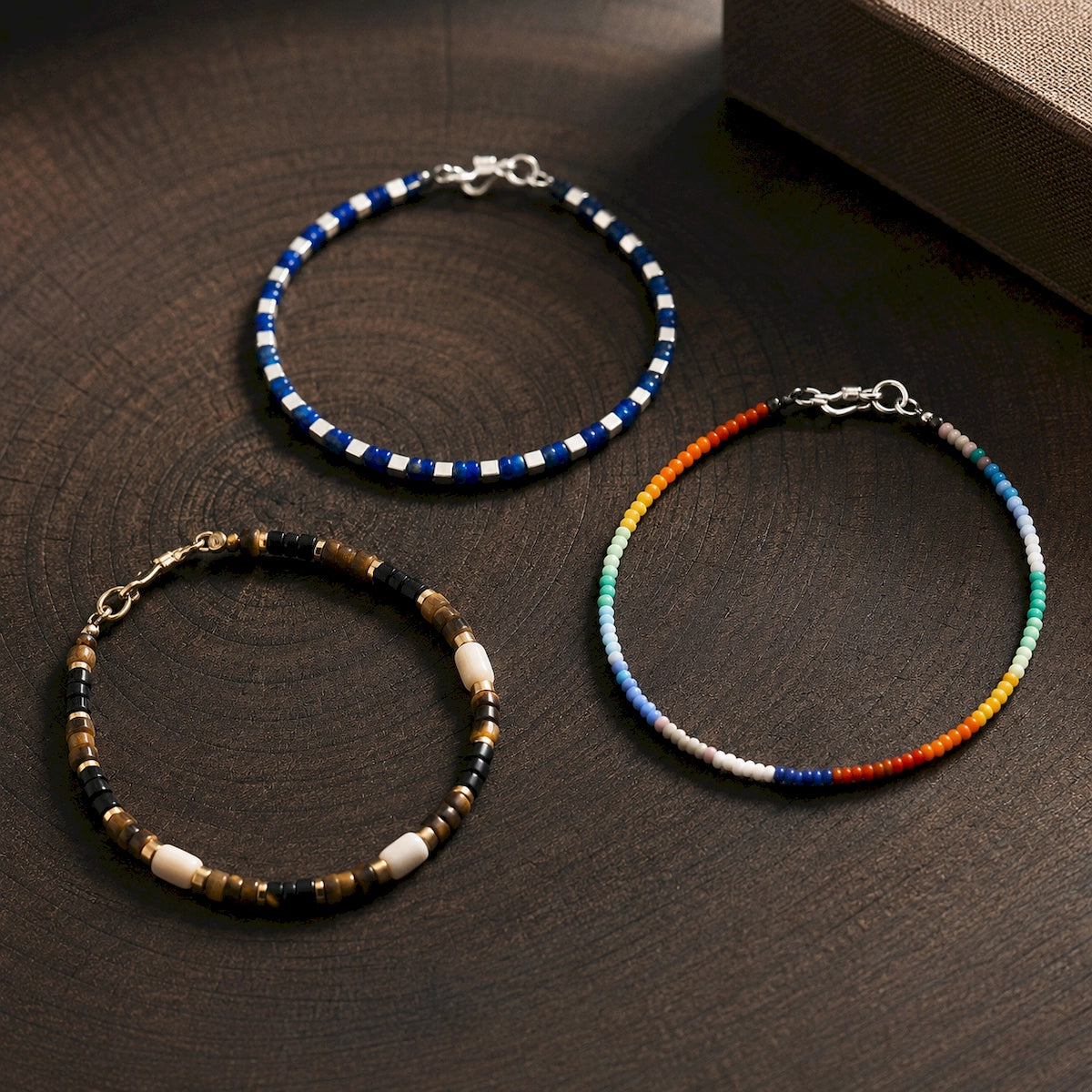Three slim men’s beaded bracelets in blue, brown and multicolor designs with metal clasps